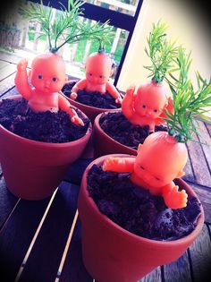 four small plastic babies in clay pots on a wooden table next to some planters