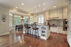 a large kitchen with white cabinets and wood flooring is pictured in this image, there are three bar stools at the center of the island