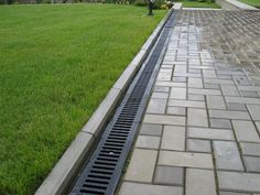 a manhole drain in the middle of a brick walkway next to a green lawn