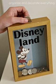 a hand holding a disney land money box with coins in it