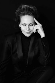 a black and white photo of a woman in a suit sitting on the floor with her hand near her face