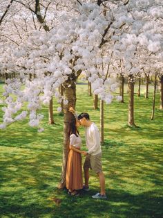 a man and woman standing next to each other in front of trees with white flowers