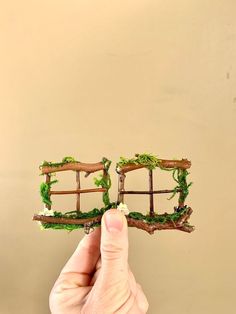 a hand holding up a miniature model of a bridge made out of branches and moss