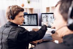 a young man wearing headphones sitting at a desk with two computer monitors in front of him