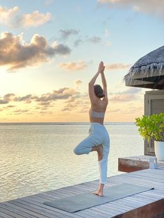 a woman doing yoga on a dock in front of the ocean