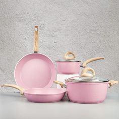 pink pots and pans with wooden handles against a gray wall, set on top of each other