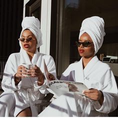 two women in bathrobes are sitting on a bench and one is holding a cup