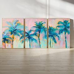 three paintings with palm trees painted in pastel colors on wood floor next to white wall