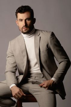 a man sitting on top of a wooden chair wearing a suit and turtle neck sweater