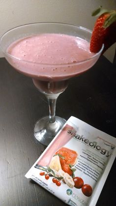 a pink drink in a glass with a strawberry on the rim next to a magazine