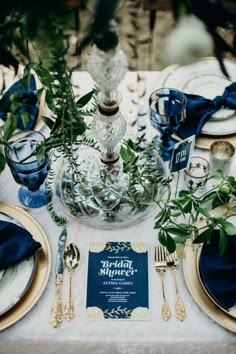 the table is set with blue and gold plates, silverware, and greenery