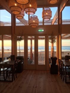 the inside of a restaurant with wooden tables and chairs, looking out onto the beach