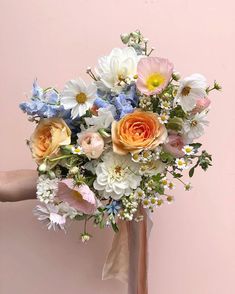 a person holding a bouquet of flowers in front of a pink wall with white and blue flowers