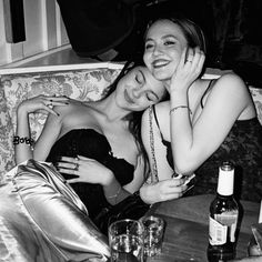 two women sitting on a couch next to each other with wine glasses and bottles in front of them