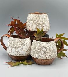 three coffee mugs sitting next to each other with leaves on the top and bottom