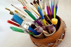 a wooden container filled with lots of different colored paintbrushes and brushes on top of a white surface