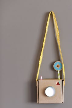 an origami camera hanging on a wall with a yellow string attached to it