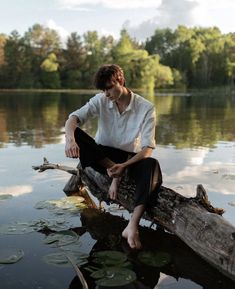 a young man sitting on top of a log in the middle of a body of water