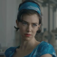 a woman with blue eyes wearing a headband and looking at the camera while standing in front of a window