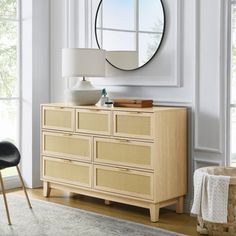 a room with white walls and a round mirror on the wall above a wooden dresser