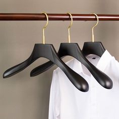 three black clothes hangers on a wooden rail next to a white button up shirt