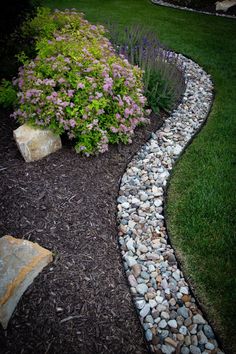 a garden with rocks and flowers in the grass next to a rock path that runs through it