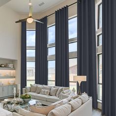 a living room filled with lots of furniture and large windows covered in blue drapes