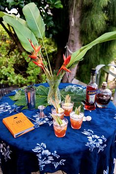 a blue table topped with glasses filled with drinks next to a plant and bottle on top of a wooden table