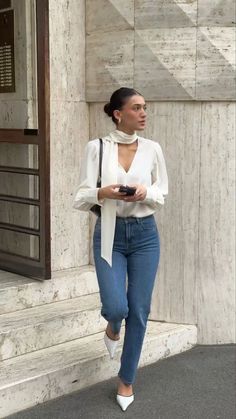 a woman is walking down the street wearing jeans and a white shirt with an open neck