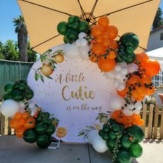 an orange and white balloon arch with the words a little cute is on the way