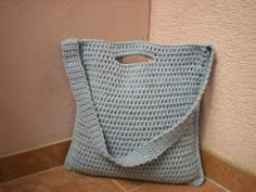 a blue crocheted bag sitting on the floor next to a pink wall with a hole in it