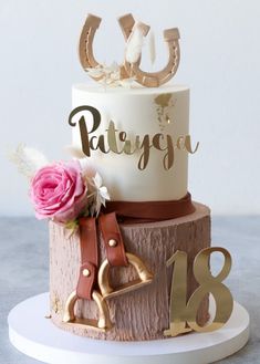 a white and gold birthday cake with pink flowers on the top is decorated with an equestrian theme