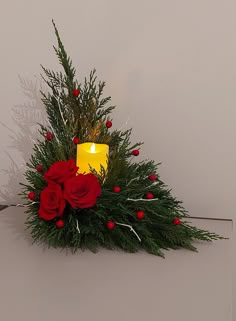 a candle and some red roses on a white surface with greenery in the corner