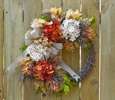 a wreath is hanging on a fence with flowers and leaves around it, as if for the fall season