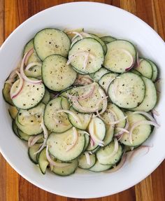 a white bowl filled with cucumbers and onions on top of a wooden table