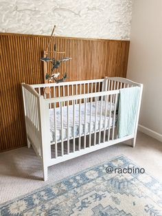 White crib against a wood slat wall. Slate Wall Nursery, Wood Slat Accent Wall Nursery, Nursery Slat Wall, Accent Wall Behind Crib, Half Wall Paneling Nursery, Wood Panel Accent Wall Nursery, Slat Wall Nursery, Wainscoting In Nursery, Nursery Chair Rail