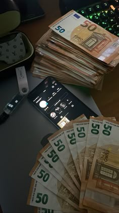 stacks of money sitting on top of a desk next to a cell phone and remote control