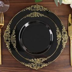 a black plate with gold trim on top of a wooden table next to silverware