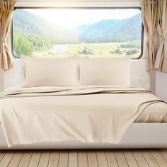 a bed with white sheets and pillows in front of a window that has mountains outside