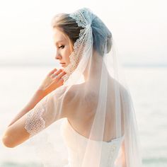 a woman in a wedding dress standing on the beach with her veil over her head