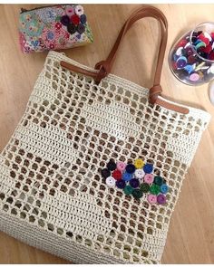 a crocheted bag with buttons on it and a purse next to it, sitting on a table