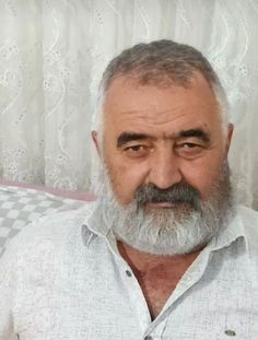 an older man with grey hair and beard sitting in front of a checkered curtain