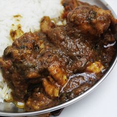 a silver plate topped with rice and meat covered in gravy on top of a white table