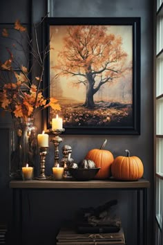 a shelf with candles and pumpkins on it in front of a framed tree print