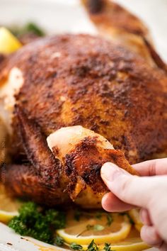 a person holding a piece of chicken on top of a white plate with lemons and parsley