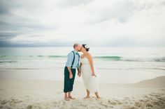 a bride and groom kissing on the beach in front of the ocean with storm clouds