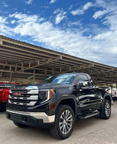 a black truck is parked in front of a large building with many other trucks behind it