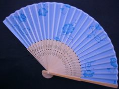 a white fan sitting on top of a wooden table next to a black background with blue flowers