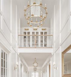 an elegant hallway with white walls and flooring, chandelier over the doorway