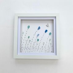 a white frame with blue and green flowers in it on the side of a wall